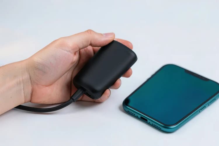 Mão segurando um carregador portátil compacto ao lado de um smartphone.