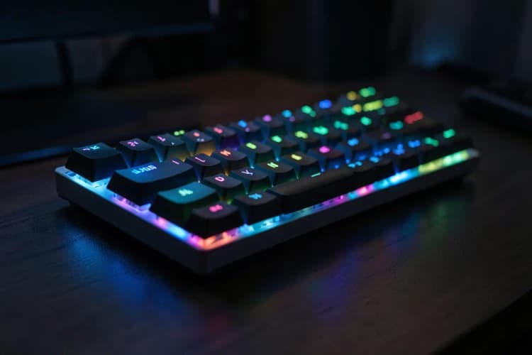 Teclado mecânico com iluminação RGB em um ambiente de trabalho com pouca luz.